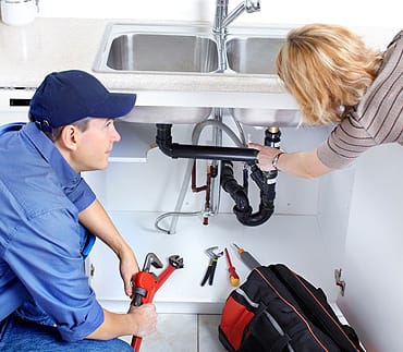 Plumber And Homeowner Repairing A Leaky Sink